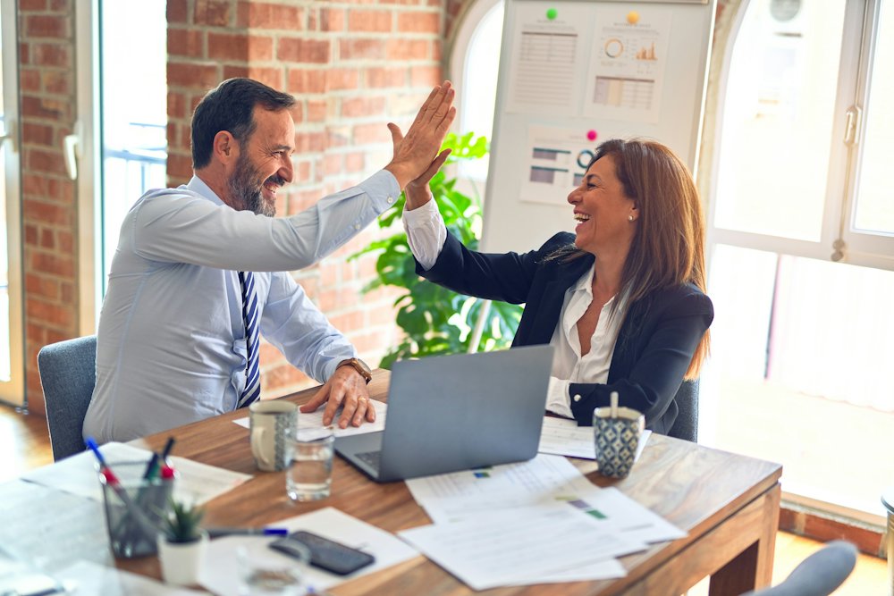 Two people at a desk celebrating with a high five